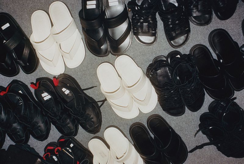 Overhead shot of assorted black and white footwear, including sandals and shoes, arranged on a light grey surface.