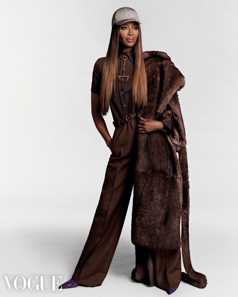 Naomi Campbell in brown jumpsuit, grey cap and fur coat poses in a studio, modelling for Vogue, fashion editorial photography.