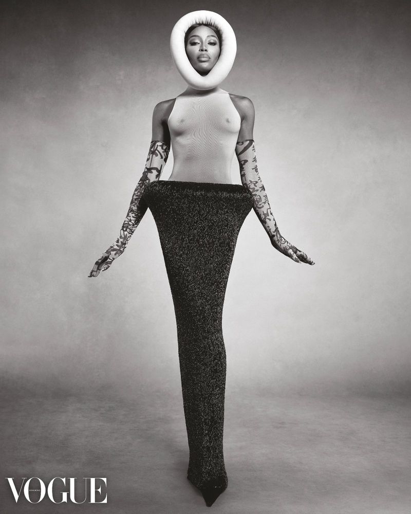Striking black and white fashion portrait of Naomi Campbell with a unique halo headpiece, gloves, and gown. Vogue magazine logo is visible.