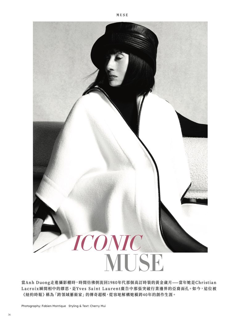Elegant editorial portrait of a woman with dark hair in a hat, wearing a white cape. Black and white tones with iconic muse text.