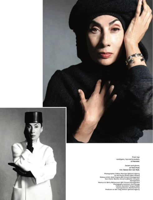 Close-up portrait of a woman with dark hair in a black beret and turtleneck, adorned with a silver bracelet, against a grey backdrop.