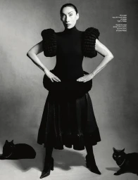 Anh Duong in a sculptural black dress posing between two black cats against a studio backdrop for Vogue Hong Kong.