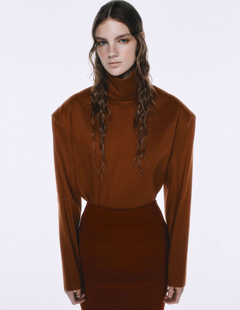 Studio shot of a young woman in a brown turtleneck and skirt against a clean white backdrop, showcasing fashion and portrait photography.