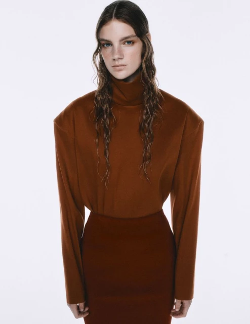 Studio shot of a young woman in a brown turtleneck and skirt against a clean white backdrop, showcasing fashion and portrait photography.