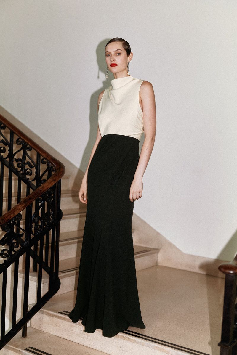 Elegant woman in sleeveless top and black skirt posing on stairs. Formal fashion shoot featuring a modern, minimalist aesthetic.