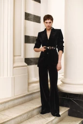 Model Greta Hofer in a black velvet belted trouser suit standing on neoclassical marble steps.
