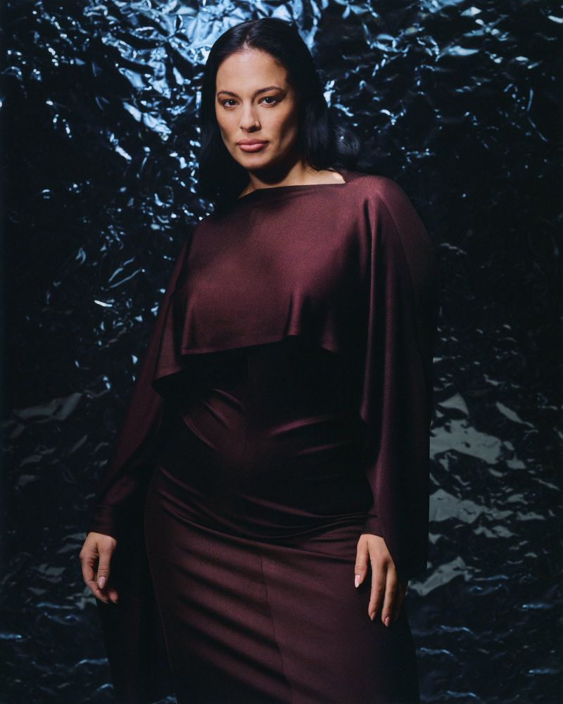 Portrait of a stylish woman in a maroon gown against a dark metallic background, captured in a studio setting with soft lighting.