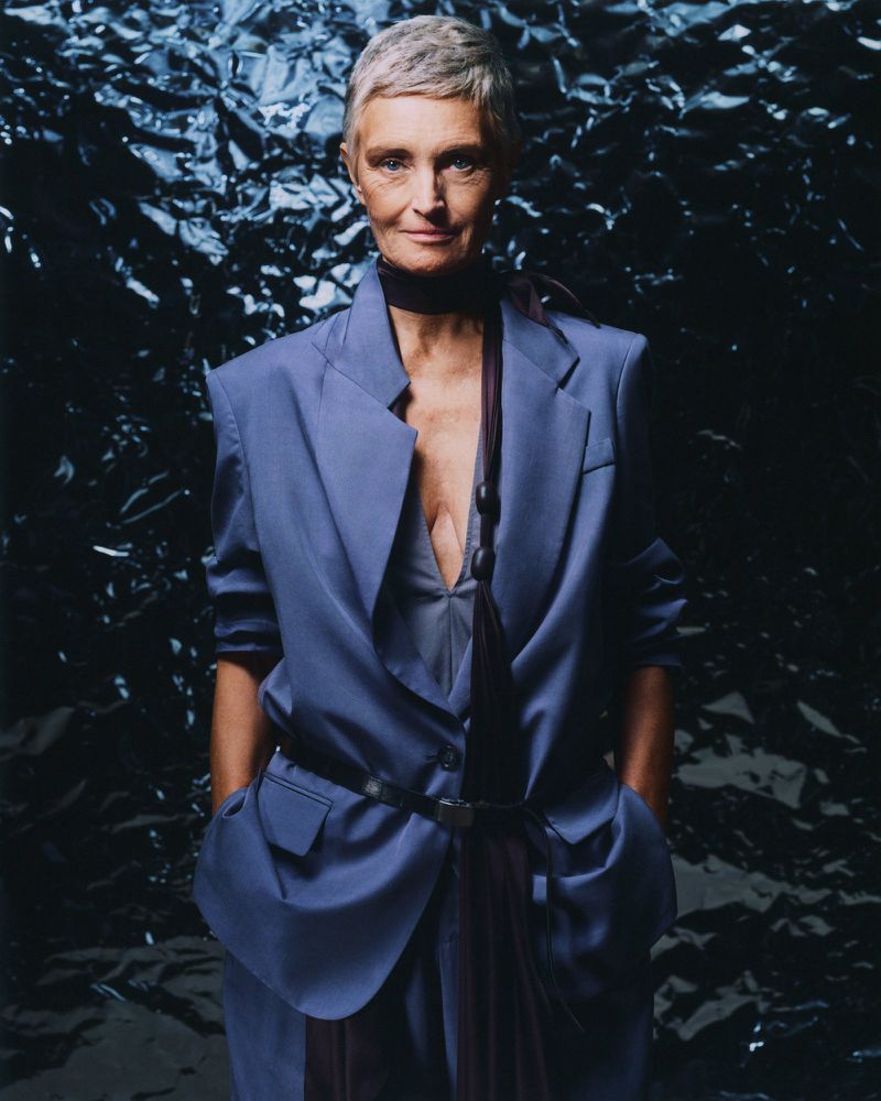 Portrait of a mature woman with short grey hair in a blue blazer with a black textured background for a fashion editorial shoot.