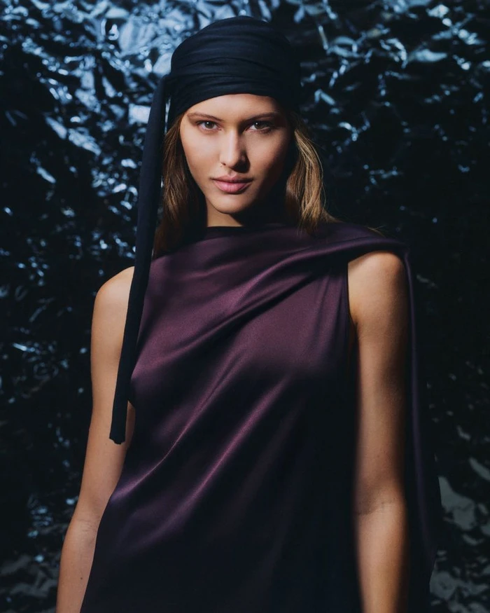 Model wearing a dark head wrap and plum-colored top against a crinkled metallic background for BOSS