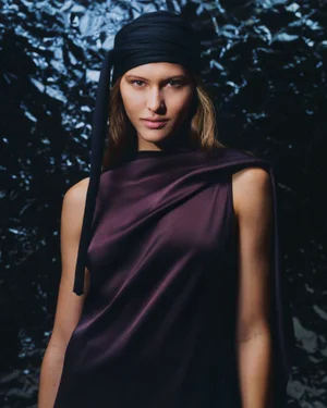 Model wearing a dark head wrap and plum-colored top against a crinkled metallic background for BOSS