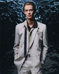 Portrait of a man wearing a light grey double-breasted suit and a dark untied necktie against a metallic textured foil background