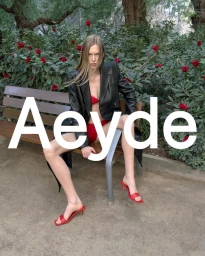 Model seated on a park bench wearing a black leather blazer and red mules in an Aeyde campaign image.