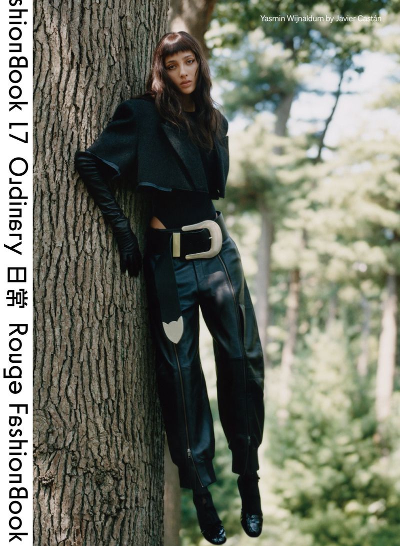 Yasmin Wijnaldum poses near a tree in an outdoor fashion editorial, wearing a black jacket, leather pants, and a large belt.