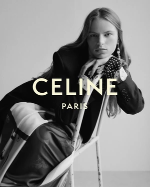 Model in a black blazer leaning on the back of a chair with draped patterned fabric in a black and white Celine campaign.