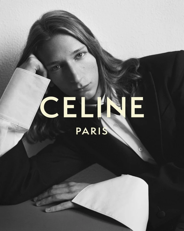 Monochrome fashion portrait of a model with long hair wearing a black jacket and oversized white cuffs, with Celine Paris text overlay.