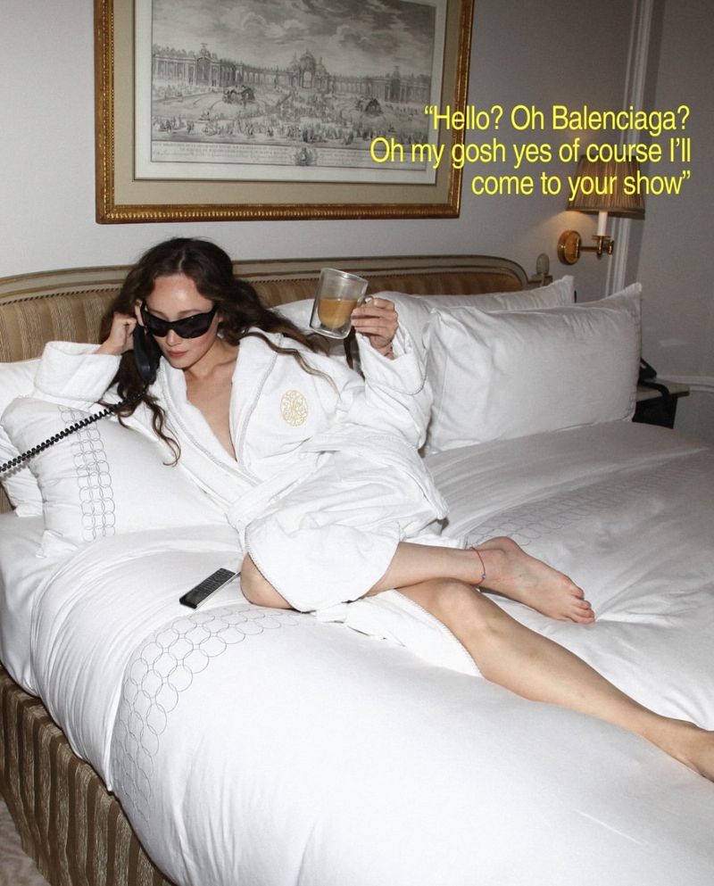 Adult female relaxing on a bed in a robe, holding a drink and a phone, with a framed picture on the wall in a hotel room.