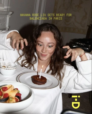 Woman in bathrobe poses playfully with a small cake and a candle on a white table; text overlay of magazine title and brand name.