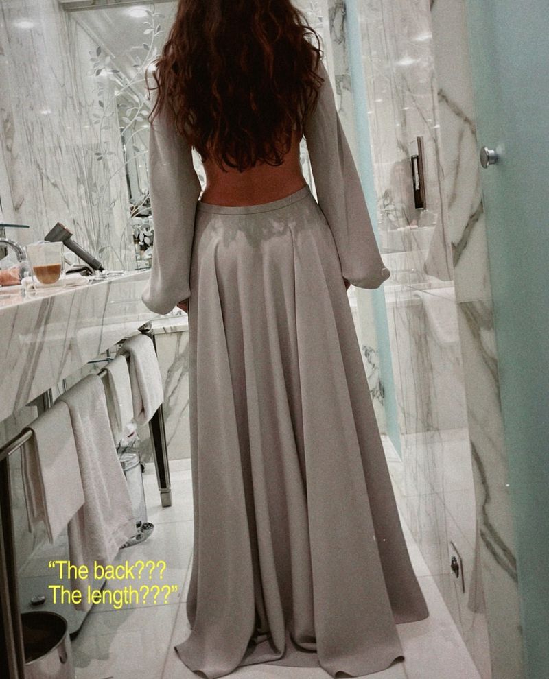 Back view of a slim adult female in a gray maxi dress with long sleeves in an indoor setting, showcasing fashion design and style.