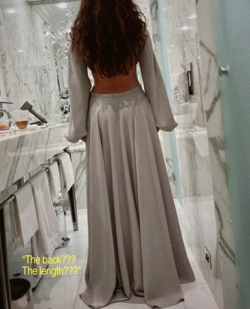 Back view of a slim adult female in a gray maxi dress with long sleeves in an indoor setting, showcasing fashion design and style.