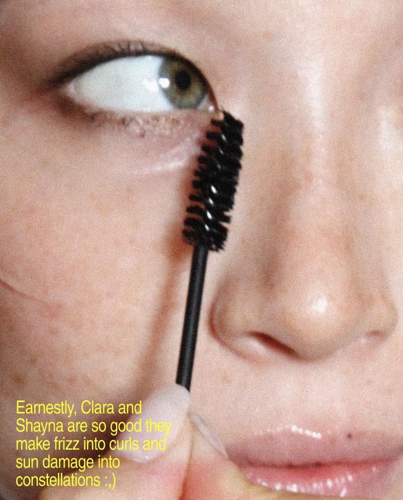 Close-up of an adult woman applying black mascara to her upper lashes. The makeup is being applied with a mascara wand.