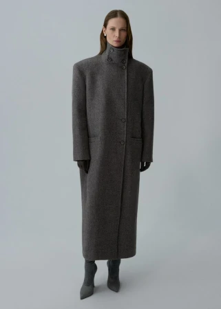 Full-length shot of an adult female model in a long grey wool coat, gloves, and grey heels, standing against a pale grey backdrop.