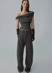 Model Angelika Wierzbicka wearing a grey off-the-shoulder structured top, matching wide-leg trousers, and dark gloves in a studio.