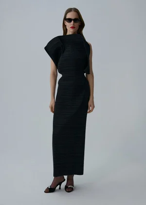 Model Angelika Wierzbicka in a structured black maxi dress with dark sunglasses and embellished mule heels against a white studio backdrop.