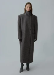Model Angelika Wierzbicka standing in a full-length charcoal grey high-neck wool coat against a grey studio backdrop.