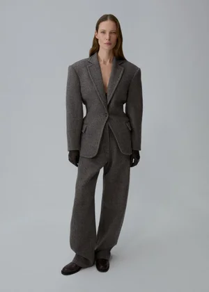 Model Angelika Wierzbicka standing in a tailored grey hourglass blazer and wide-leg trousers against a light grey studio background.