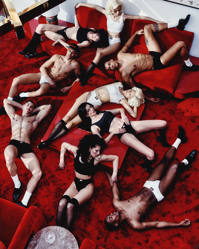 Group of diverse young adults in underwear and activewear posing in an indoor setting on a red surface, top-down view, studio lighting.