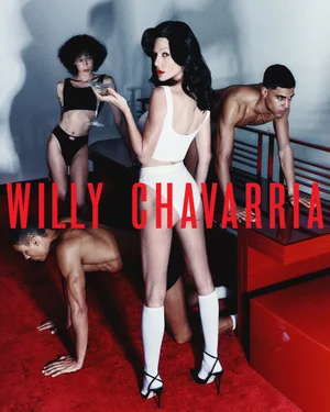 Model in white underwear and knee-high socks holding a cocktail amid several figures on a red carpet for Willy Chavarria