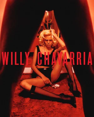 Model with blonde hair seated on red carpet wearing black underwear set and heels framed between dark legs