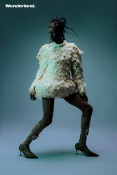 Model wearing a textured cream mini dress and pointed heels posing against a teal blue studio background for Wonderland.