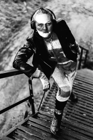 Lana Nikcevic wearing headphones and a leather jacket posing on an outdoor slatted metal staircase in high-contrast black and white.