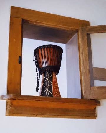 Close-up of a Djembe drum, decorated with geometric patterns, sitting inside of a rustic wooden window frame against a white wall.