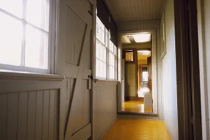 Brightly lit vintage wooden hallway with panelling, large windows, and a yellow painted floor leading into adjoining rooms.