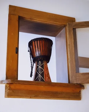 A decorative djembe drum placed inside an open wooden wall cabinet with a glass door against a white wall.