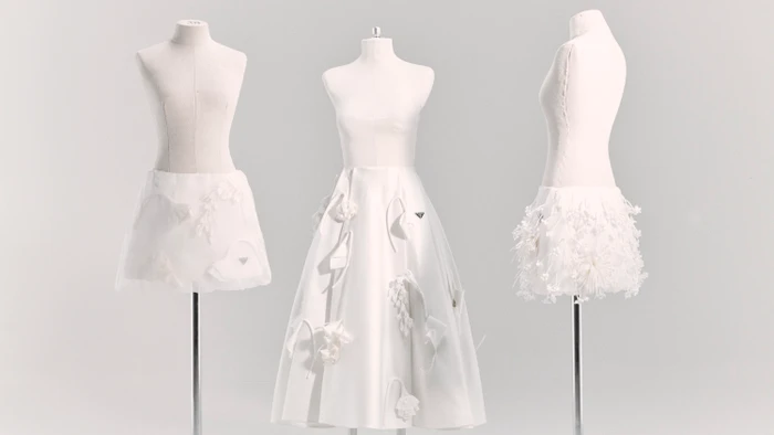 Three white tailor mannequins displaying white Prada skirts with 3D floral embellishments against a pale seamless studio background.