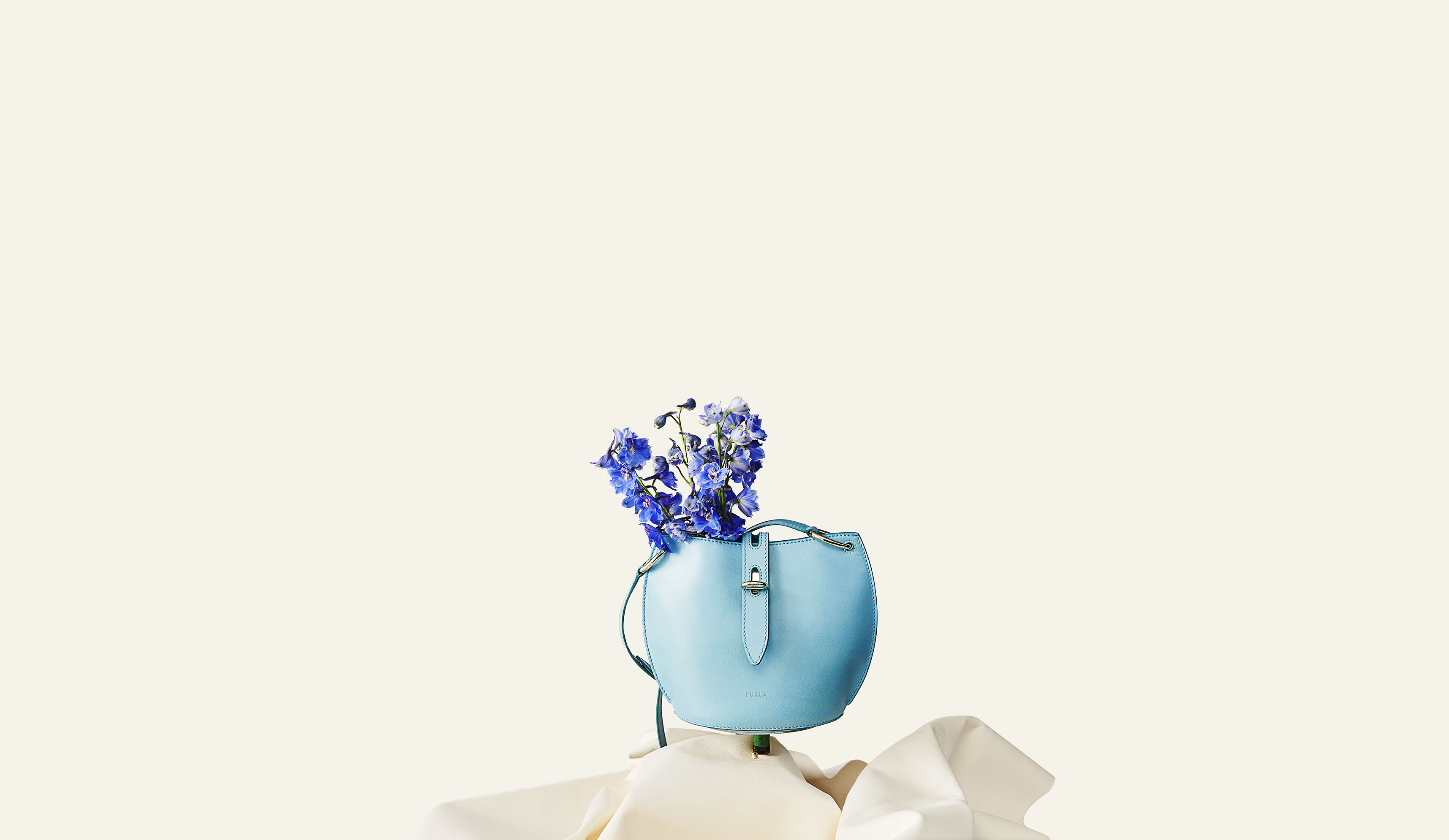 Turquoise leather Furla handbag with blue flowers placed on a white cloth, positioned in the center against a cream background.
