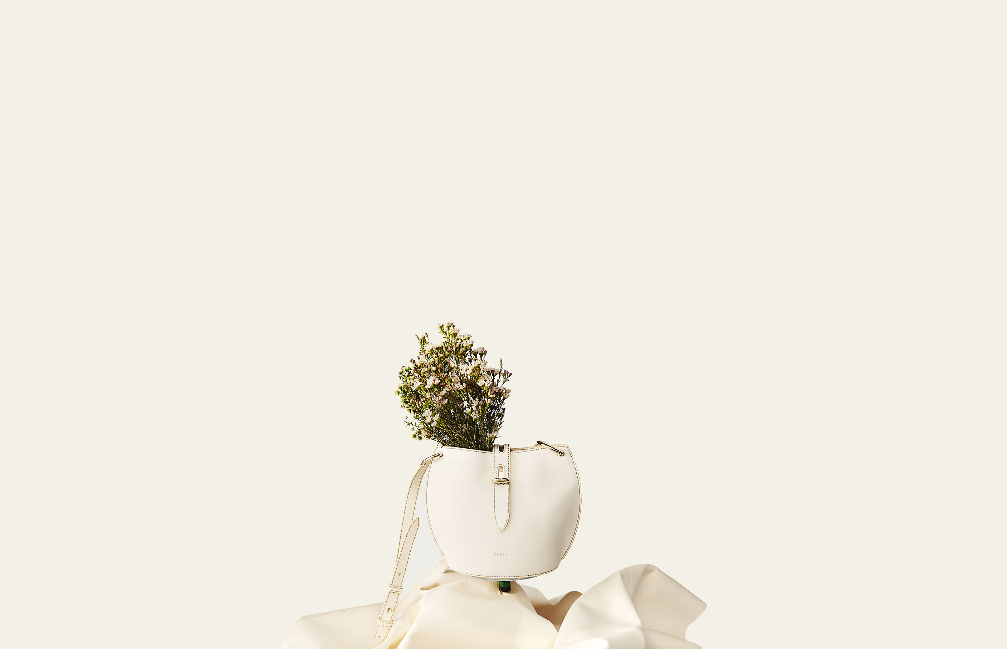Cream-colored purse with flowers, shot in a studio environment. The handbag is displayed on a soft, draped, matching material.