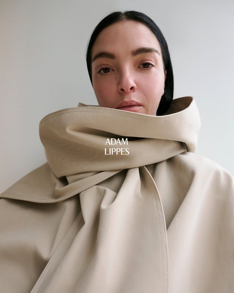 Close-up of an adult woman in a cream-colored coat with a high collar that frames her face against a plain light background.
