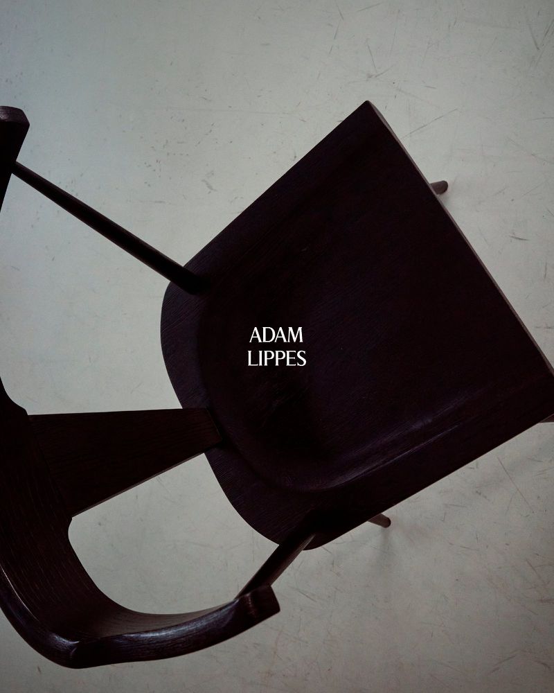 Minimalist photo of a dark brown chair against a light grey backdrop, focusing on the chair's design and color contrast.