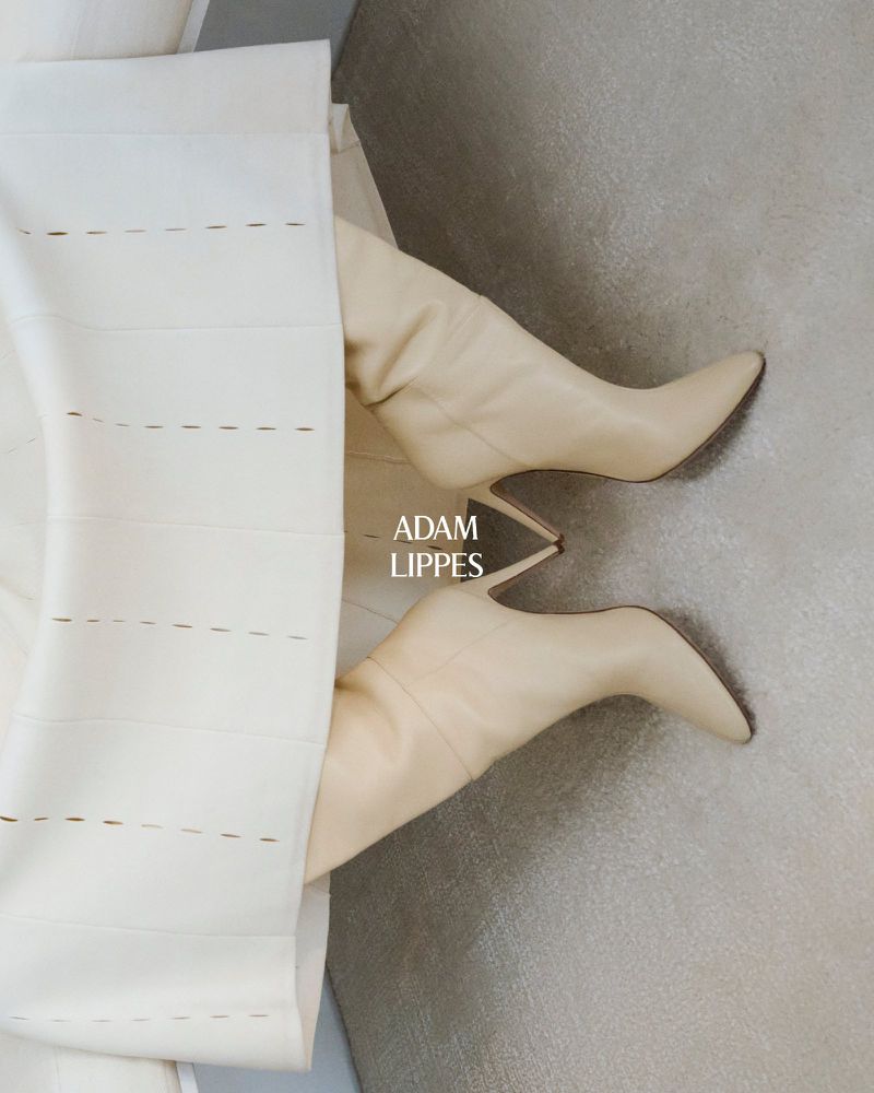 Beige stiletto heel boots under an ecru dress with textured stripe detail, set against a neutral-toned background. Minimalist fashion shot.