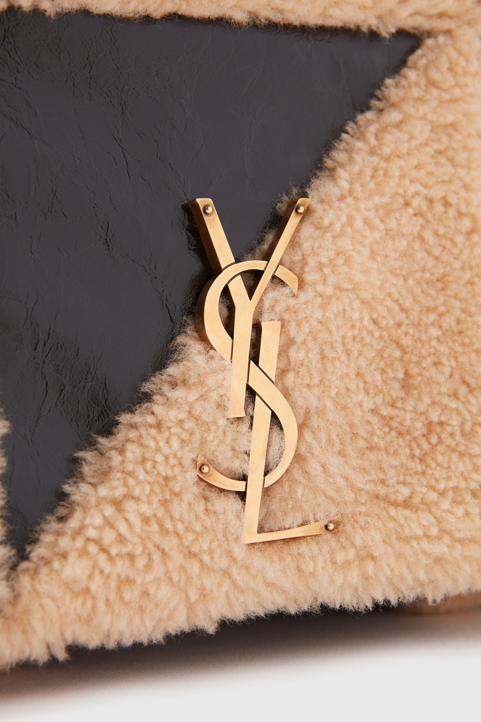 Saint Laurent handbag with fuzzy shearling and leather, featuring a gold YSL logo, displayed in a close-up studio shot.