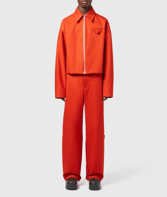 Person wearing a bright orange jacket with zipper and matching orange wide leg pants. Fashion shot in a neutral studio setting.