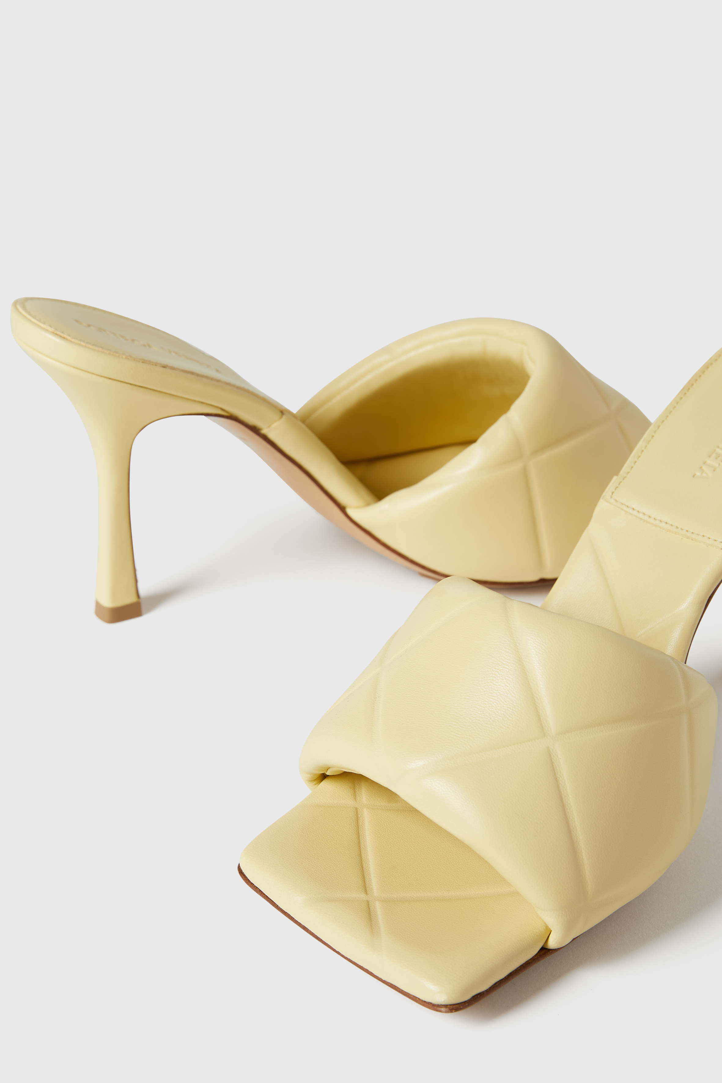 Pair of light yellow leather heeled sandals with a quilted pattern on a white background in a studio product shot. Fashionable footwear.