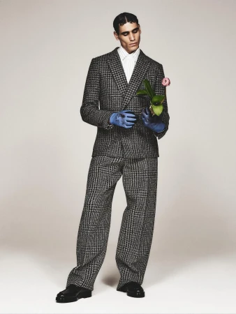 Man in a houndstooth suit holds a flowering plant in blue gloves. Fashion shot on a neutral background. Portrait with plant and formalwear.