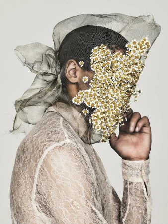 Conceptual portrait of a person wearing lace and mesh with flowers covering their face, set against a light background.