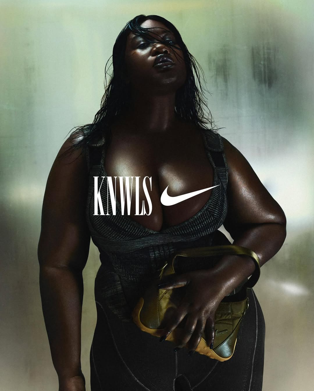 Fashion portrait of an African American female model in a low-cut top, holding a purse against a muted background in a studio setting.