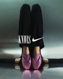 Two pairs of legs in black trousers wearing metallic pink sneakers against a reflective grey studio backdrop.